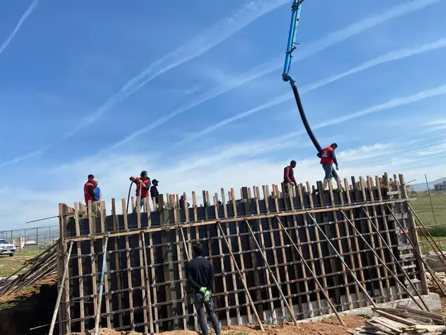 Construction workers pouring concrete into wooden formwork using a concrete pump, with a clear blue sky in the background.