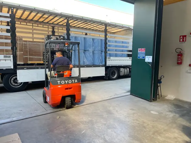 Forklift loading materials onto a truck at a construction site warehouse.