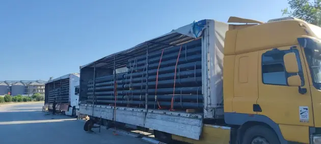 Large-scale delivery of pipes for a major construction project, with multiple trucks loaded.